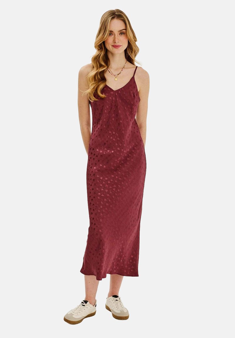 Bordová saténová šaty s textúrovaným vzorom, s tenkými ramienkami a midi dĺžkou. Nosí sa s bielymi teniskami, s uvoľneným strihom.