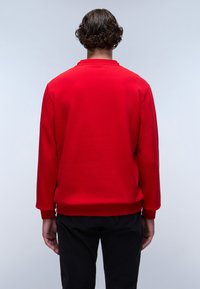 Sudadera roja de mangas largas, con puños y cuello acanalados. Textura suave y color sólido, llevada con pantalones negros. Se muestra la vista trasera.