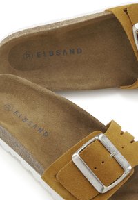 Sandales en suede marron avec une large sangle, une boucle en argent et une semelle en liège. Semelle extérieure en caoutchouc blanc ; le dessous présente "ELBSAND" imprimé en bleu.
