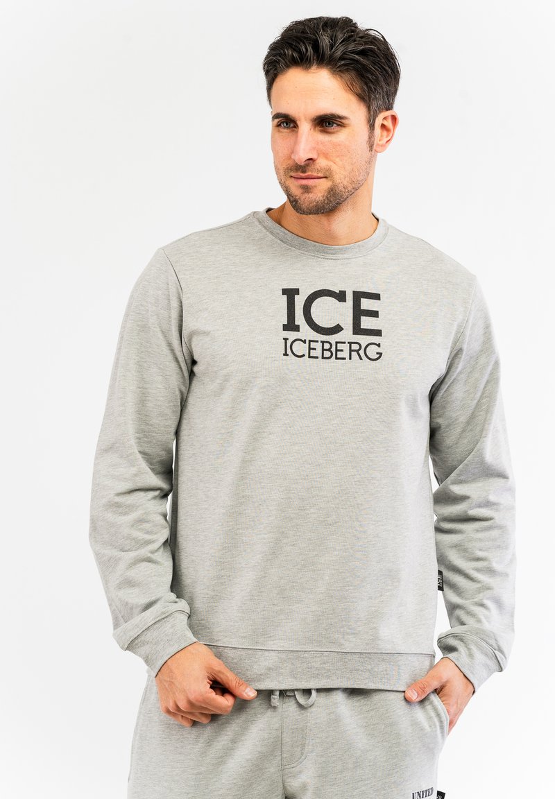 Svijetlosiva dukserica s dugim rukavima, rebrastim manžetama i donjim rubom. Na prednjem dijelu ima veliki crni grafički natpis "ICE ICEBERG". Meko na dodir.