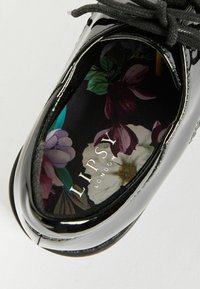 Interno di scarpa in pelle verniciata nera con motivo floreale e marchio "LIPSY LONDON". Punta arrotondata e lacci piatti. Imbottitura confortevole.