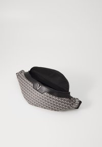 Svartvit midjeväska med geometriskt mönster, med läderkant, dragkedja och metallaccent med bokstaven "V".