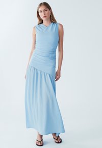 Gaiši zilas krāsas gara kleita bez piedurknēm ar piegulošu bodiju, rievotu tekstūru un plūstošu svārku. Valkāta kopā ar melnām čībām.