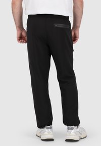 Zwarte sportbroek met een elastische tailleband, voorzien van een ritszak aan de achterkant en taps toelopende pijpen. Gladde textuur, ademend materiaal.