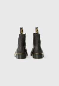 Bottines en cuir noir avec une finition texturée, des coutures jaune clair et des languettes comportant le texte "WITH Bouncing". Semelle plate en caoutchouc.