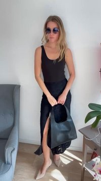 Sort ærmeløs top og lang sort nederdel med slids. Modellen holder en sort taske, bærer solbriller og lyse sko. Enkel, strømlinet design.