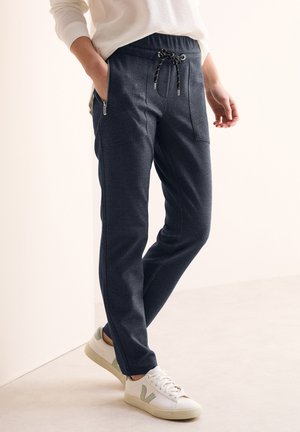 Jogging en bleu nuit en tissu texturé, avec taille à cordon, poches latérales zippées et une coupe fuselée.