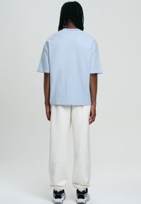 Ljusblå bomulls t-shirt med korta ärmar, avslappnad passform. Tillsammans med vita sweatpants och svarta sneakers med grå detaljer.