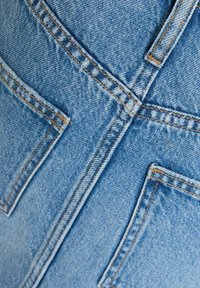 Primo piano di un tessuto di denim azzurro chiaro che mostra cuciture incrociate e due tasche posteriori con cuciture arancioni.