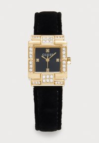 Gouden vierkante Guess-horloge met een zwarte fluwelen band, een zwarte wijzerplaat, kristallen uurmarkeringen en kristallen accenten op de bezel.