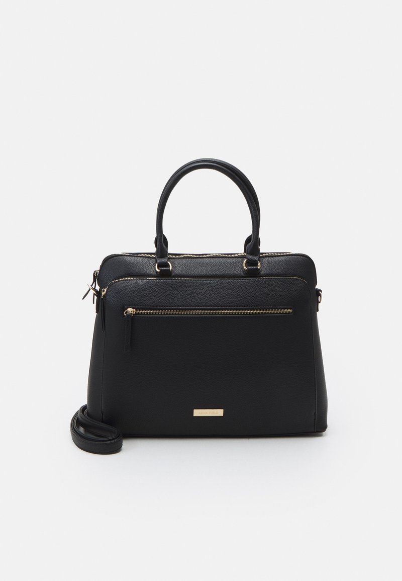 Sac à main en cuir noir avec double poignée, poche avant zippée, bandoulière amovible, fermeture éclair et plaque logo dorées sur fond blanc.