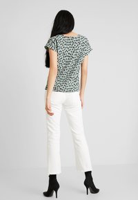 Zelený top s černými nepravidelnými skvrnami, lehký materiál, krátké rukávy, kulatý výstřih, doplněný o bílé zvonové džíny a černé vysoké boty na podpatku.