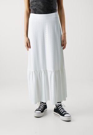 Woman wearing white ankle-length eyelet skirt, black sleeveless top, and black high-top sneakers with white laces.