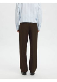 Brune, vide bukser med glatt tekstur, kombinert med en lyseblå stripete skjorte. Enkel design, figursydd passform i midjen.