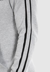 Grijze sweatshirtmouw met een textuurstof en zwarte zijstreep. Het ontwerp heeft een lichtgetailleerde vorm en ribboord.