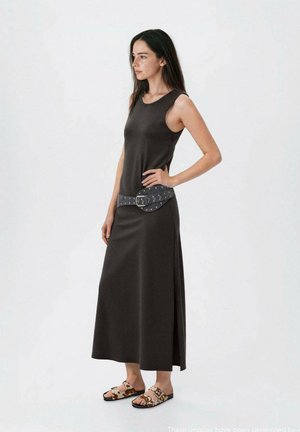 Abito maxi senza maniche di colore grigio scuro con uno spacco laterale. Abbinato a una cintura larga con accessori in argento e sandali con stampa.
