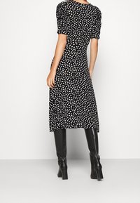 Černé midi šaty s bílými puntíky, s nafouknutými rukávy a přiléhavým korzetem. Stylizované s černými vyššími botami a hladkou texturou.
