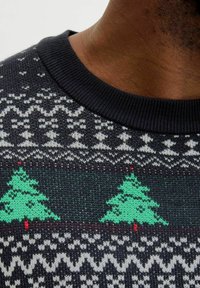 Zwarte trui met witte en groene kerstboomontwerpen, een textuurpatroon van gebreid materiaal, een geribbelde kraag en decoratieve accenten.