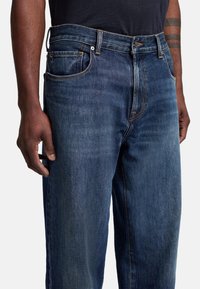 Granatowe dżinsy z prostą nogawką, z pięcioma kieszeniami, delikatnym przetarciem i kontrastowymi szwami wzdłuż szwów.