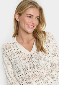 Strickpullover in Creme mit offenem Blattmuster, V-Ausschnitt und geripptem Kragen. Lange Ärmel; weiche Textur und leichtes Design.