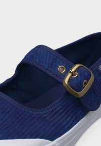 Μπλε υφασμάτινο παπούτσι Mary Jane με χρυσό λουράκι αγκράφα και λευκή καουτσούκ σόλα, φωτογραφία από κοντά με γωνία.