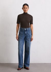 T-shirt marron à col roulé court associé à un jean bleu taille haute à jambes larges avec poches avant et bottines marron.
