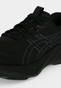Μαύρο αθλητικό παπούτσι ASICS με σκούρες γκρι λωρίδες λογότυπου, μαλακή σόλα και δεμένα κορδόνια σε λευκό φόντο.