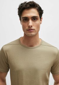 T-shirt a maniche corte color marrone chiaro in tessuto morbido, con scollatura rotonda e cuciture sottili, caratterizzata da una texture liscia e un design aderente.