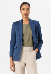 Meriinoblå blazer med en fitted design, notched lapeller og enkeltknaplukning, parret med en olivengrøn top og beige bukser.