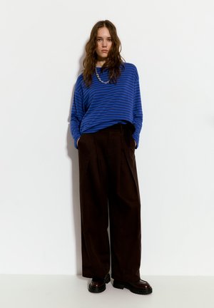 Top a maniche lunghe a strisce blu abbinato a pantaloni larghi a vita alta marroni, caratterizzati da una consistenza liscia e scarpe nere robuste.
