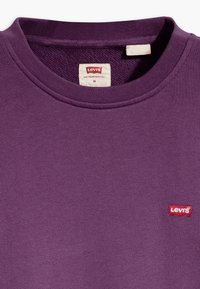 Sweat-shirt violet avec un col côtelé, présentant une petite étiquette logo Levi's rouge sur le côté gauche. Fabriqué en tissu doux et texturé.