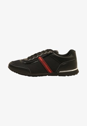 Baskets basses noires avec lacets noirs, bande latérale rouge marquée "Versace Jeans," et accent blanc au talon de la semelle.