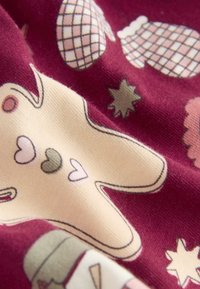 Bomullstyg i djup burgundy med ett krämfärgat pepparkaksgubbsdesign, hjärtan, stjärnor och mönstrade vantar med mjuk textur.