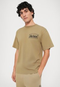 Olijfgroene t-shirt van katoen, met een ontwerp met korte mouwen, ronde hals en een zwart "Aries" logo op de linker borstzak.
