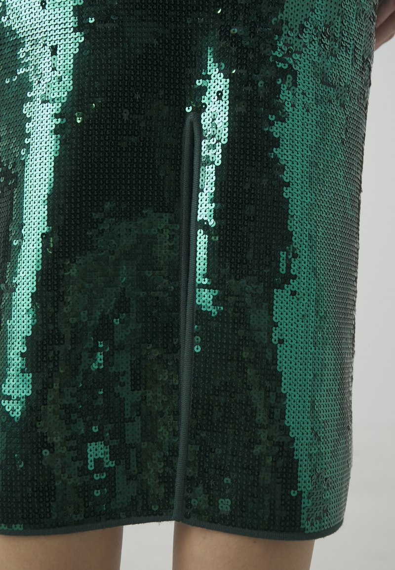 Zielona spódnica z cekinami o gładkim kroju z rozcięciem z przodu, błyszczącą fakturą i gładką podszewką.