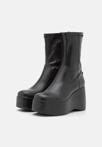 Bottines à plateforme en cuir noir avec fermeture éclair, dotées d'un bout arrondi et d'un talon compensé épais pour plus de hauteur et de stabilité.