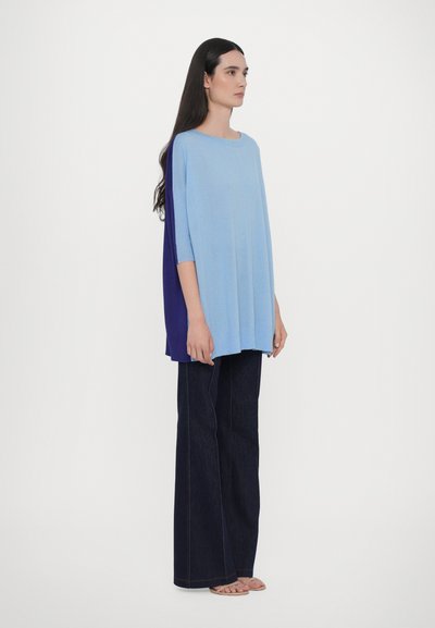 Top larg, cu mâneci scurte, de culoare albastru deschis și albastru închis, asortat cu pantaloni largi din denim închis. Textură netedă, design minimalist.