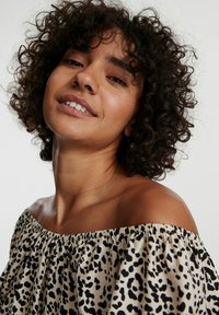 Schulterfreies Blusenshirt aus leichtem Stoff mit einem Leopardenmuster in Schwarz und Beige, mit einem gerafften Ausschnitt und weicher Textur.