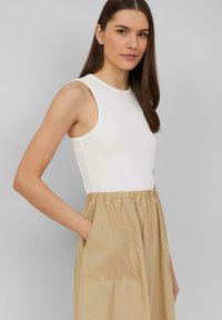 White sleeveless top with a round neckline, paired with a high-waisted beige skirt featuring an elastic waistband and side pockets.