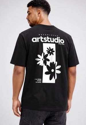Mann trägt ein schwarzes T-Shirt mit weißen Blumengrafiken und dem Text "artstudio," "neverless," und "true design around the world" auf dem Rücken.