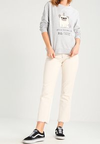 Felpa grigia con grafiche di carlini e testo, abbinata a jeans cropped di colore chiaro e sneakers nere con accenti bianchi.