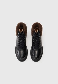 Botas de invierno de cuero negro con suelas de goma gruesas, cordones negros y un forro de piel marrón alrededor del cuello del tobillo, vistas desde arriba.