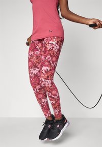 Maroon kukkia leggings, joissa on vaaleanpunaisia yksityiskohtia, valmistettu joustavasta kankaasta. Yhdistetty mustiin urheilu kenkiin, joissa on vaaleanpunaisia yksityiskohtia ja logo.