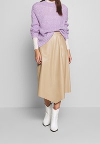 Violetti neulepaita, beige tekonahkahame, valkoiset nilkkasaappaat. Neulepaita on löysästi istuva; hameessa on epäsymmetrinen helma.