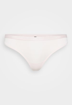 Bílé tanga vyrobené z měkké tkaniny, s elastickým světle růžovým pasem s embosovanou značkou, minimálním šitím a hladkými okraji.