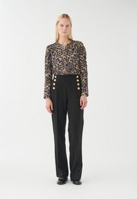 Blumenbluse in Marineblau und Gold mit Puffärmeln und Knopfleiste. Hochgeschnittene schwarze Hose mit goldenen Knöpfen am Bund.