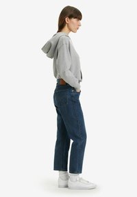 Felpa grigia, jeans in denim blu e scarpe da ginnastica bianche. I jeans hanno una vestibilità comoda e tasche posteriori visibili. Design semplice, senza fantasie.