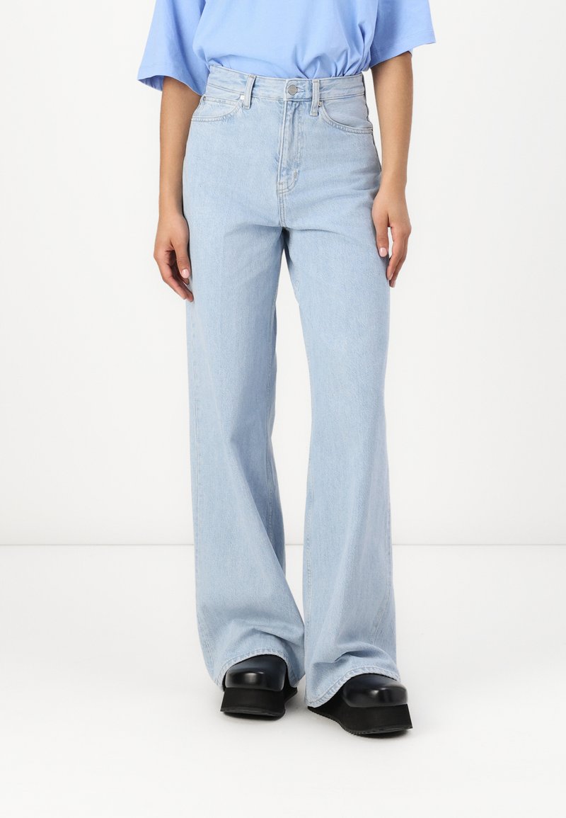 Ljust blå högmidjade utsvängda jeans med en ren design, subtila sömmars detaljer och vida benöppningar, kompletterat av svarta platåskor.