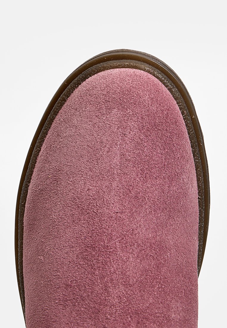 Zapato de ante rosa con punta redondeada y superficie texturizada, que cuenta con una suela de goma marrón. Acabado suave con un diseño minimalista.