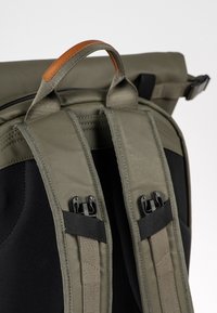 Bretelles rembourrées vertes pour sac à dos avec clips de boucle noirs et une poignée de transport supérieure avec un détail en cuir marron.